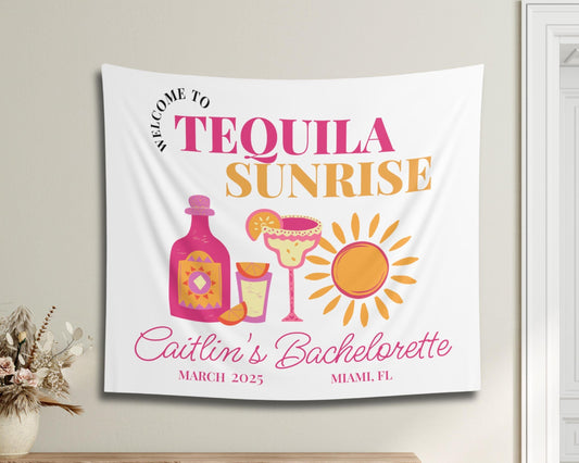 May include: A white tapestry with pink and yellow text and illustrations. The text reads &#39;Welcome to Tequila Sunrise Caitlin&#39;s Bachelorette March 2023 Miami, FL&#39;. The illustration includes a bottle of tequila, two margarita glasses, a slice of orange, and a sun.